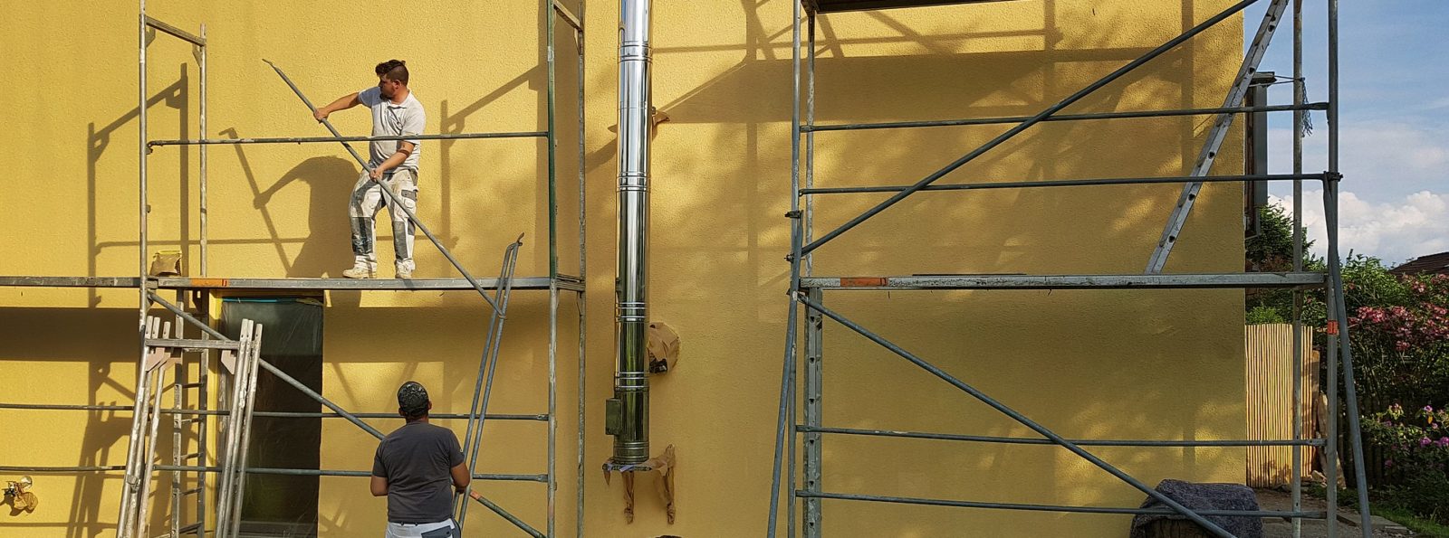 Dwóch mężczyzn przy rusztowaniu obok żółtej ściany.